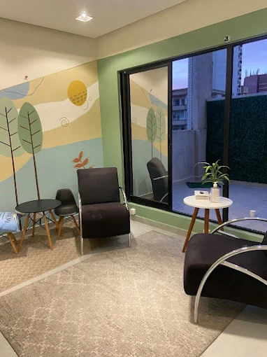 Canto do consultório com duas poltronas, mesa com planta e janela ampla