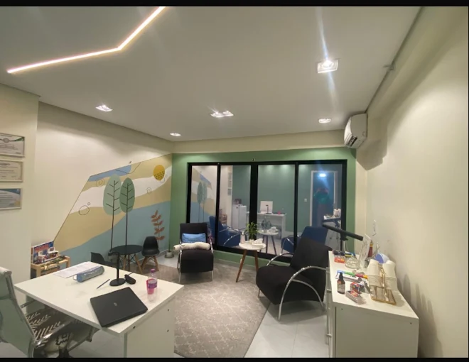 Sala de atendimento com mural de árvores e sol, poltronas pretas e parede verde-sálvia