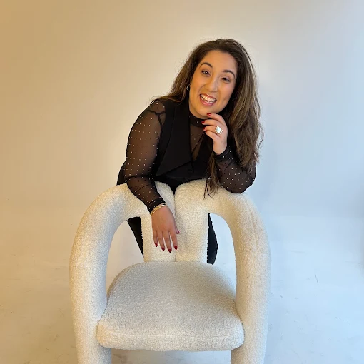 Flor Gonzalez sorrindo, apoiada em uma poltrona bouclé branca